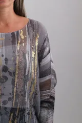Sweter de punto con diseño abstracto en tonos grises, negros y detalles metalizados dorados. Presenta cuello redondo, mangas tres cuartos y un corte holgado.