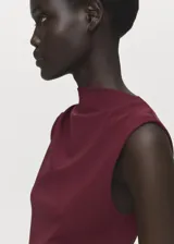Vestido midi de color bordó, sin mangas, con cuello redondo y diseño entallado. Presenta un detalle de fruncido lateral en la cintura y cierre posterior.