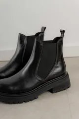 Bota Chelsea de cuero negro con elástico lateral y suela track.