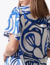 Blusa de seda fría con estampado abstracto en blanco y azul. Tiene cuello redondo con frunce, escote en V con botón y mangas cortas amplias.