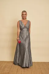 Vestido largo gris metalizado, con escote en V profundo, sin mangas y corte en la cintura con falda amplia.
