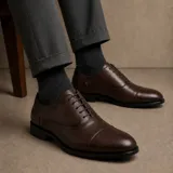 Zapato tipo Oxford de cuero sintético color marrón oscuro, con diseño de puntera reforzada y cordones al tono. Cuenta con suela de goma antideslizante.