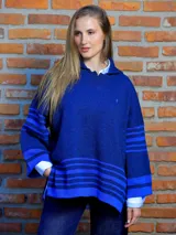 Poncho de lana con mangas, diseño holgado y cuello con capucha. Presenta detalles de franjas horizontales en tonos azules en las mangas y en el ruedo.