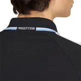 Campera deportiva adidas de la Selección Argentina, color negro con cierre frontal, cuello tipo polo con detalles en celeste y blanco, y las icónicas tres tiras blancas en las mangas. Presenta el logo de adidas Originals a la derecha y el escudo de la AFA a la izquierda.