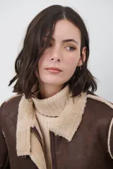 Chaquetón de efecto cuero en color marrón, con interior y detalles en corderito color bordó. Presenta cierre frontal con cremallera y botones a presión, cuello solapa y mangas largas con puños de corderito.