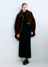 Vestido largo negro de punto con cuello alto, manga larga y detalle de aplique metálico dorado en la cintura.
