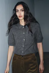 Chaqueta de punto con textura cepillada, cuello polo y manga corta. Presenta cierre frontal con botones y diseño de corte recto.