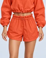 Conjunto deportivo de dos piezas color durazno, compuesto por un buzo cropped de manga larga con cuello alto ajustable y cintura regulable, y un short con cintura clochard y cordones laterales.