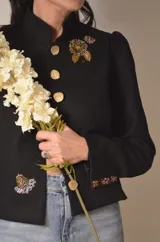 Chaqueta de terciopelo azul marino con hombreras marcadas, mangas largas y bordados florales plateados en el frente. Presenta un diseño estructurado con cierre frontal de botones.