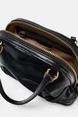 Bolso mini de mano color negro con acabado brillante, diseño estructurado y herrajes dorados. Cuenta con asas de mano fijas y cierre superior mediante cremallera.