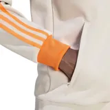 Campera deportiva Adidas Originals del Bayern de Múnich, color beige claro (Wonder Alumina) con detalles en naranja vibrante, cuello alto, cierre frontal y franjas en las mangas.
