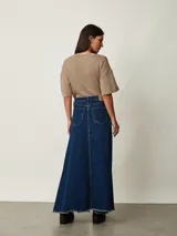 Pollera larga de denim azul con diseño de paneles, bolsillos delanteros y tajo frontal. Presenta terminación deshilachada en el ruedo.