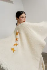 Ruana de tejido de punto color crudo, con flecos en el ruedo y apliques de estrellas bordadas a mano en tonos dorados y ocres.