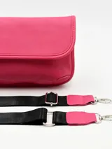 Bolso tipo bandolera de color fucsia, con solapa frontal y correa ajustable de tela negra.