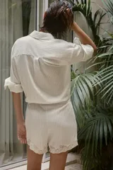 Mono corto camisero de mezcla de lyocell con estampado de rayas finas, cuello solapa, manga larga y cierre frontal con botones. Presenta cintura elástica y detalles de encaje en el bajo.