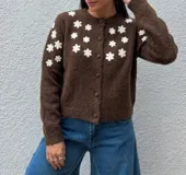 Cardigan de punto color marrón con textura suave, cuello redondo y cierre frontal con botones forrados. Presenta un diseño de flores blancas bordadas en la parte superior delantera y en las mangas.