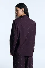 Blazer de sarga color bordó con corte oversize, hombreras marcadas y cierre frontal con un botón forrado a tono. Presenta un diseño estampado de cuadrícula con detalles de hotfix y bolsillos frontales con solapa.