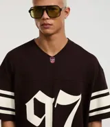 Remera deportiva de algodón color marrón con cuello en V y mangas cortas. Diseño overboxy con estampado de fútbol americano, lettering y rayas contrastantes en blanco.