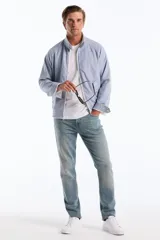 Campera estilo Harrington de corte clásico con diseño de rayas finas verticales en tono celeste y blanco. Cuenta con cuello alto, cierre frontal completo, bolsillos diagonales con solapa y botones, además de puños y dobladillo elastizados. Presenta el logo bordado del pingüino característico en el pecho.