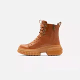 Bota de caña media Sorel, confeccionada en cuero impermeable color marrón tostado. Presenta un diseño moderno con cordones frontales, herrajes metálicos en forma de D y una suela de caucho robusta con plataforma dentada. Incluye tirador en el talón y cierre lateral para mayor practicidad.
