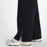 Pantalón deportivo ancho (wide leg) color negro, con cintura elástica a rayas blancas y un pequeño logo cuadrado de New Balance en la cadera.