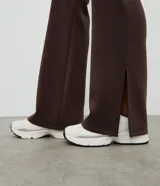 Pantalón deportivo de corte flare, color marrón, con cintura elástica y diseño liso. Presenta una abertura lateral en el bajo.
