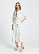 Vestido camisero midi blanco con estampado floral, cuello camisero, mangas 3/4 abullonadas, cierre frontal con botones y lazo ajustable en la cintura.