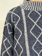 Sweater de lana color bordó con cuello alto y diseño de rombos y líneas verticales en rojo. Tiene puños y dobladillo acanalados.