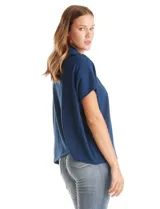 Cardigan de punto azul, con cierre frontal metálico completo, cuello con solapa y mangas cortas de sisa caída. Presenta un corte recto y holgado.