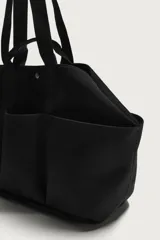 Bolso shopper negro fabricado en tejido técnico, con compartimento principal con cierre de botón a presión, múltiples bolsillos exteriores frontales, doble asa de mano y asas largas de hombro.