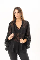 Blusa negra de tejido semitransparente con diseño floral en relieve, cuello alto con lazo frontal y mangas largas con volados en los puños.