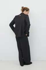 Blazer de corte sastrero en color gris oscuro, con cierre frontal de un botón, solapas clásicas y bolsillos con solapa. Presenta una estructura entallada y hombreras marcadas.