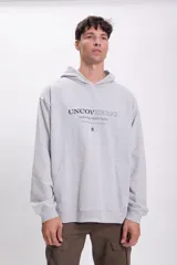 Canguro deportivo gris claro con capucha y bolsillo tipo canguro. Estampado frontal con la frase "Uncovering revealing hidden truths" y un pequeño logo.