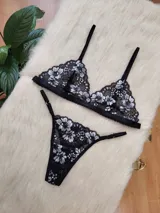 Conjunto de lencería compuesto por un bralette triangular y una bombacha tipo tanga, confeccionados en encaje negro con detalles florales en hilo plateado.