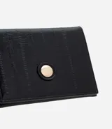 Billetera pequeña tipo sobre de la marca Satinato, confeccionada en poliuretano texturizado color negro. Presenta un diseño compacto con cierre de botón metálico dorado y un interior organizado con divisiones para tarjetas.