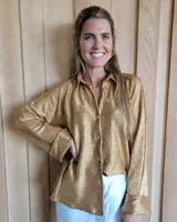 Camisa de corte holgado en color dorado con acabado brillante y textura plisada. Presenta cuello clásico, cierre frontal con botones y mangas largas con puños anchos doblados.