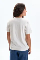 Remera de manga corta color crudo con estampado frontal que dice "Café Lumière" en cursiva y "Open All Week" debajo.