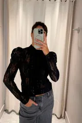 Camisa de encaje negro con cuello alto, mangas largas con hombreras abullonadas y diseño ajustado.