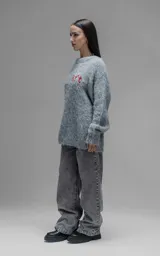 Sweater de punto texturizado color gris, con cuello redondo y diseño oversize. Presenta un bordado en relieve en la espalda con la frase 'art SUPPORT' en letras rojas y negras.