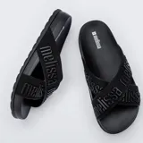Sandalias Melissa modelo Cozy Slide M Lover II, de color negro, con suela anatómica y tiras cruzadas de tela con el nombre de la marca en relieve.
