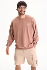 Buzo deportivo sin friza color marrón claro, con cuello redondo, mangas largas, puños y cintura elásticos, y pequeño texto estampado en el pecho.