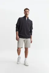 Buzo de tejido de punto color verde oliva, con cuello alto y cierre frontal parcial. Presenta un pequeño logo bordado en el pecho.