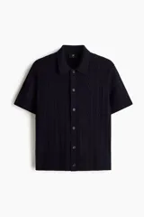 Camisa en punto trenzado de mezcla de algodón, modelo de manga corta con cuello, cierre frontal de botones y bajo recto con remate acanalado.