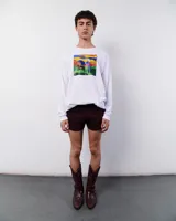 Remera blanca de manga larga, confeccionada en algodón. Presenta un estampado rectangular con una ilustración de un hombre con su caballo en un paisaje montañoso.