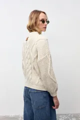 Sweater de tejido de punto grueso color crudo, con diseño de trenzas frontales, cuello redondo y mangas largas con puños ajustados.