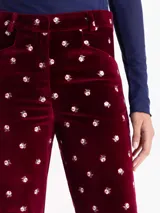Pantalón de terciopelo color bordó con estampado floral en blanco y verde. Diseño de corte recto, con cierre frontal, gancho y botón interno. Incluye bolsillos delanteros horizontales, bolsillos ojal en la espalda y presillas en la cintura para cinturón.