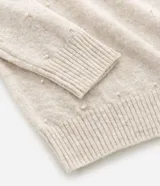 Suéter de punto color beige con cuello redondo, manga larga y aplicaciones de perlas distribuidas por toda la prenda. Presenta puños y ruedo acanalados.