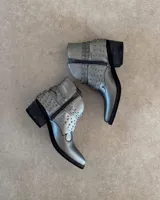Botines cortos plateados de cuero vacuno, con punta fina, taco bajo y detalle de tachas y correas alrededor del tobillo.