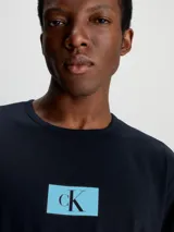 Conjunto de pijama Calvin Klein compuesto por una remera de manga larga negra con logo CK en el pecho y un pantalón largo negro con estampado del logo CK en azul.