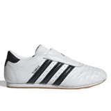 Championes Adidas modelo Taekwondo, color blanco con las icónicas tres tiras laterales en negro. Presentan un diseño minimalista sin cordones, con una lengüeta que cubre el empeine y suela de goma color caramelo.